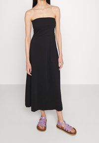 Svart strapless maxiklänning med en figurnära bodice och flödande kjol. Kombinerad med bruna och lavendelfärgade sandaletter med remmar. Mjuk textur.