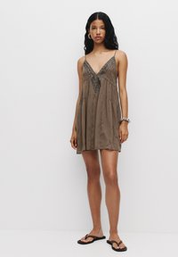 Rochie maro fără mâneci, cu decolteu în V și detalii decorative cu mărgele, având un design fluid și țesătură texturată. Purtați cu sandale.