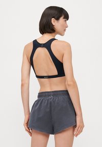 Reggiseno sportivo nero con design racerback e chiusura con gancetto. Abbinato a pantaloni corti grigi con cordoncino. Logo discreto sul retro.