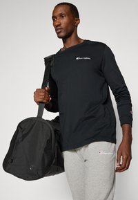 Black long-sleeve shirt with white "Champion" logo, gray sweatpants, and a black duffel bag with zipper and side vents.