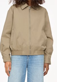 Beige lightweight jacket with a collared neck, elastic waistband, and side pockets. Features a front zipper and smooth, matte texture.