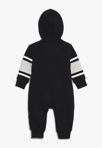 Zwarte jumpsuit met capuchon, voorzien van lange mouwen met grijze stof en witte strepen. De zachte textuur en ribgebreide manchetten verhogen het comfort.