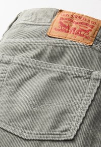 Grijze corduroy broek met achterzak en een tan kleurige leren patch van Levi Strauss & Co. gestikt boven de zak.