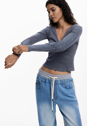 Haut gris côtelé à manches longues avec un col en V, associé à un pantalon de survêtement en denim bleu clair ample avec une taille élastique et un cordon de serrage.