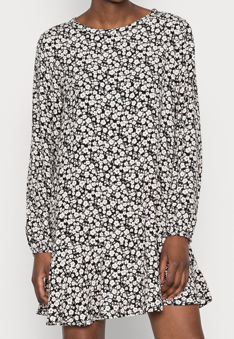 Langarmige zwarte jurk met een wit bloempatroon, ronde halslijn en een uitlopende zoom. Gemaakt van lichtgewicht stof met een gestructureerde afwerking.