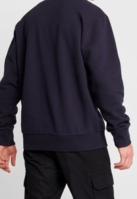 Sudadera azul marino con puños y dobladillo acanalados, con un escote de barco y una textura suave, vista desde la parte de atrás.
