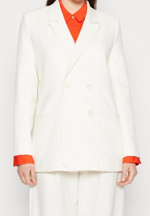 Vit dubbelknäppt blazer med spetsiga slag, sidofickor och röda manschetter, tillverkad av ett slätt, strukturerat tyg.