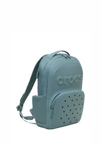 Jasnoniebieski plecak Crocs z wyściełaną kieszenią z przodu, posiadającą otwory wentylacyjne oraz regulowane szelki.