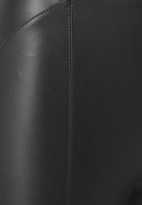 Svarta leggings i konstläder med en slät textur, som har en central söm och en subtil lyster. Nära vy som framhäver materialet och formen.