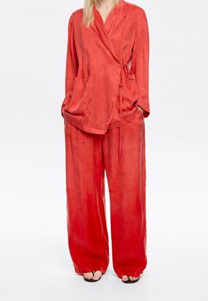 Rode, loszittende loungewear set van zacht materiaal. De top heeft een wikkelontwerp met twee voorzakken en een gestrikt taille.