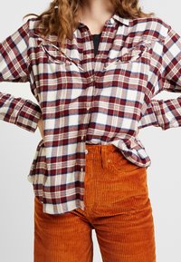 Rotes und weißes karriertes Flanellhemd mit Knopfleiste, langen Ärmeln und zwei Brusttaschen, kombiniert mit strukturierten orangefarbenen Cordhosen.