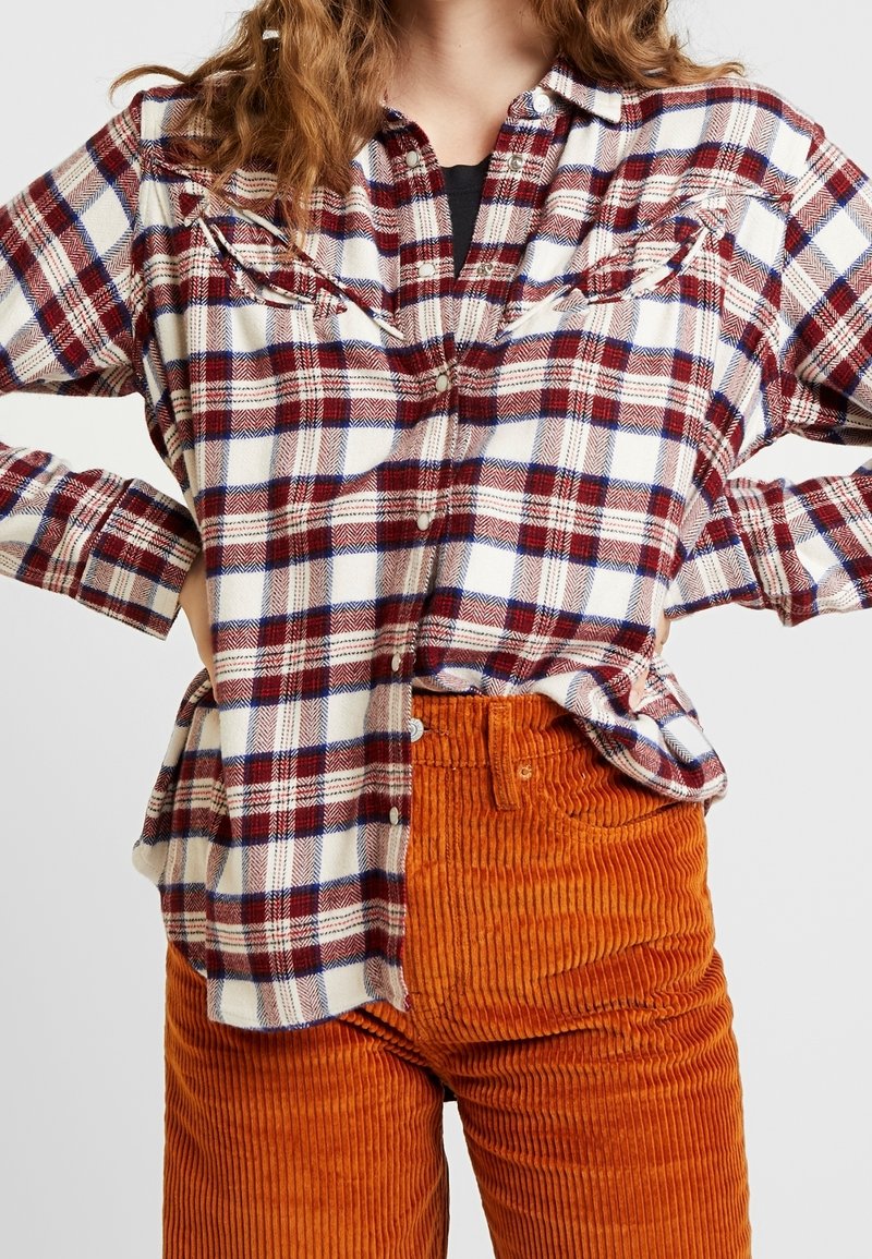 Rotes und weißes karriertes Flanellhemd mit Knopfleiste, langen Ärmeln und zwei Brusttaschen, kombiniert mit strukturierten orangefarbenen Cordhosen.