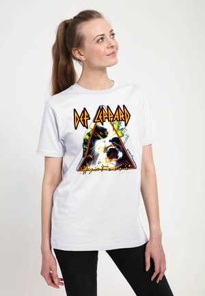 Ung kvinde med brunt hår i en hestehale bærer en hvid Def Leppard band t-shirt med et farverigt grafik- og tekstdesign.