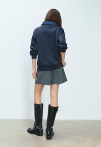 Námořnická mikina s deninovým límcem, šedá sukně s jemným proužkem a černé kozačky nad kolena. Hladká tkanina a přiléhavý design.