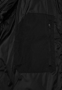 Sort nylon stof med en syet firkantet lomme, der har en lodret lynlås på højre side.