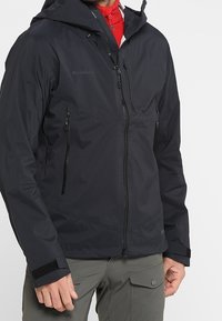 Sort vandtæt jakke med hætte, der har lynlåslommer og justerbare manchetter. Glat tekstur med et minimalistisk design.