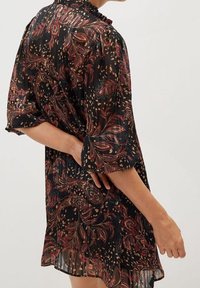 Vestido negro con pliegues y patrones florales y de paisley en tonos rojos, rosas y dorados. Presenta un cuello volado y mangas cortas anchas.