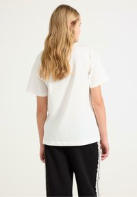 Vit bomull t-shirt med korta ärmar, avslappnad passform och rak nederkant. Matchas med svarta sweatpants med sidodetaljer.