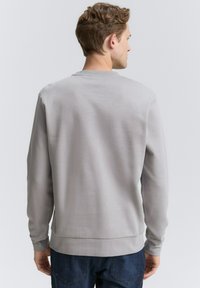 Lichtgrijze sweatshirt met een ronde hals en ribbels aan de mouwen en onderkant. Glad oppervlak, geen patronen of logo's zichtbaar vanuit het achteraanzicht.