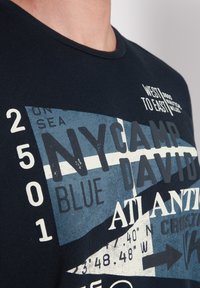 Camiseta de algodón azul oscura con diseños gráficos en blanco y azul claro, que incluyen texto y formas geométricas. Cuello redondo.