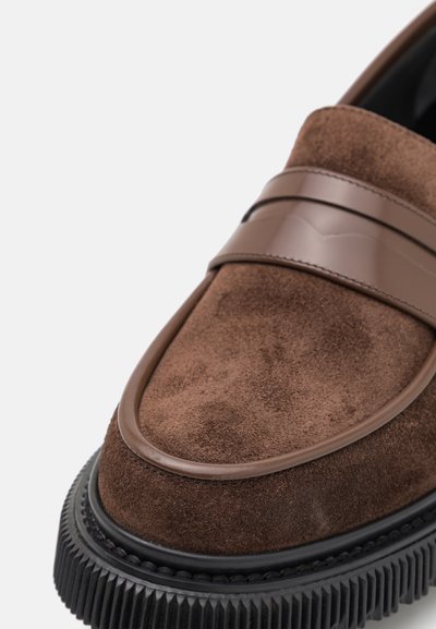 Brūni zamšādas loafers ar spīdīgu brūnu joslu, noapaļotu purngalu un strukturētu melnu gumijas zoli ar rieviņām.