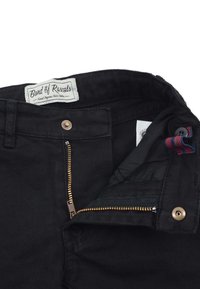 Svarta denimbyxor med en gyllene dragkedja, knäppning med knapp, och en etikett som läser "Band of Rascals." De har en slät yta och fickor.