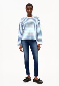 Maglietta a righe blu e bianche a maniche lunghe, taglio rilassato; abbinata a jeans scuri aderenti; scarpe nere rifinite con frange.