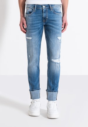 Vaqueros de mezclilla azul claro con un corte ajustado, que presentan detalles desgastados y puños enrollados, combinados con zapatillas blancas.
