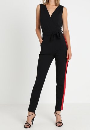 Woman wearing a sleeveless black jumpsuit with a V-neck, waist belt, red side stripes, and black strappy high-heeled sandals.