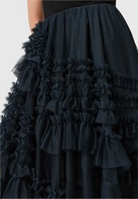 Gonna in tulle nera con volant a strati e fiocchi, creando un aspetto strutturato. Il tessuto è leggero e trasparente.