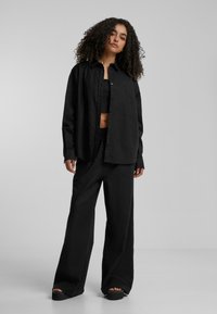 Black oversized shirt with buttons, and matching loose-fit trousers. The outfit is made of a smooth fabric, featuring a cropped tank underneath.