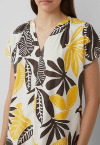 Korte mouwen witte shirt met zwarte en gele bladpatronen. V-hals ontwerp met een ontspannen pasvorm en een natuurlijke stofstructuur.