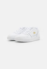 Baskets blanches avec dessus en cuir lisse, semelle en caoutchouc, lacets plats, détails perforés sur les côtés et petit logo doré sur le côté extérieur.