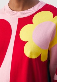 Maglione multicolore con un grande fiore giallo e sezioni rosse e rosa. Ingrandimento del collo a costine e del tessuto di cotone testurizzato.