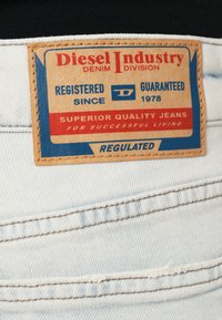 Bežist nahast täpp heledenimis teksapükstel, millel on punane ja sinine tekst. Tekst sisaldab brändi, registreerimise ja kvaliteedi teavet.