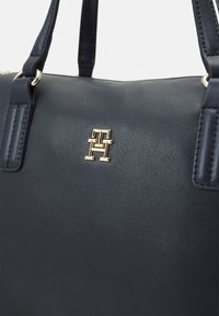 Navyblaue Lederhandtasche mit strukturierter Form, Logo-Detail in Goldtönen und stabilen Riemen. Glatte Textur mit Nahtakzenten.
