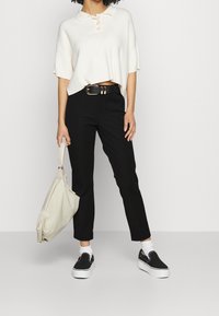 Polo de punto crema con mangas cortas, combinado con pantalones negros ajustados, calcetines blancos, zapatos negros sin cordones y un bolso beige.