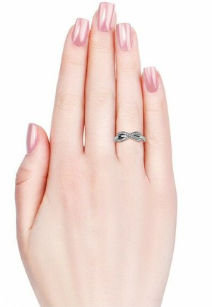 Anello infinito in argento con piccole decorazioni nere, esposto su una mano con smalto rosa chiaro. Superficie liscia e design delicato.