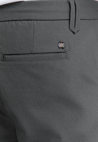 Grijze broek met een gladde textuur, voorzien van een achterzak en een klein hexagonvormig metalen accent nabij de tailleband.