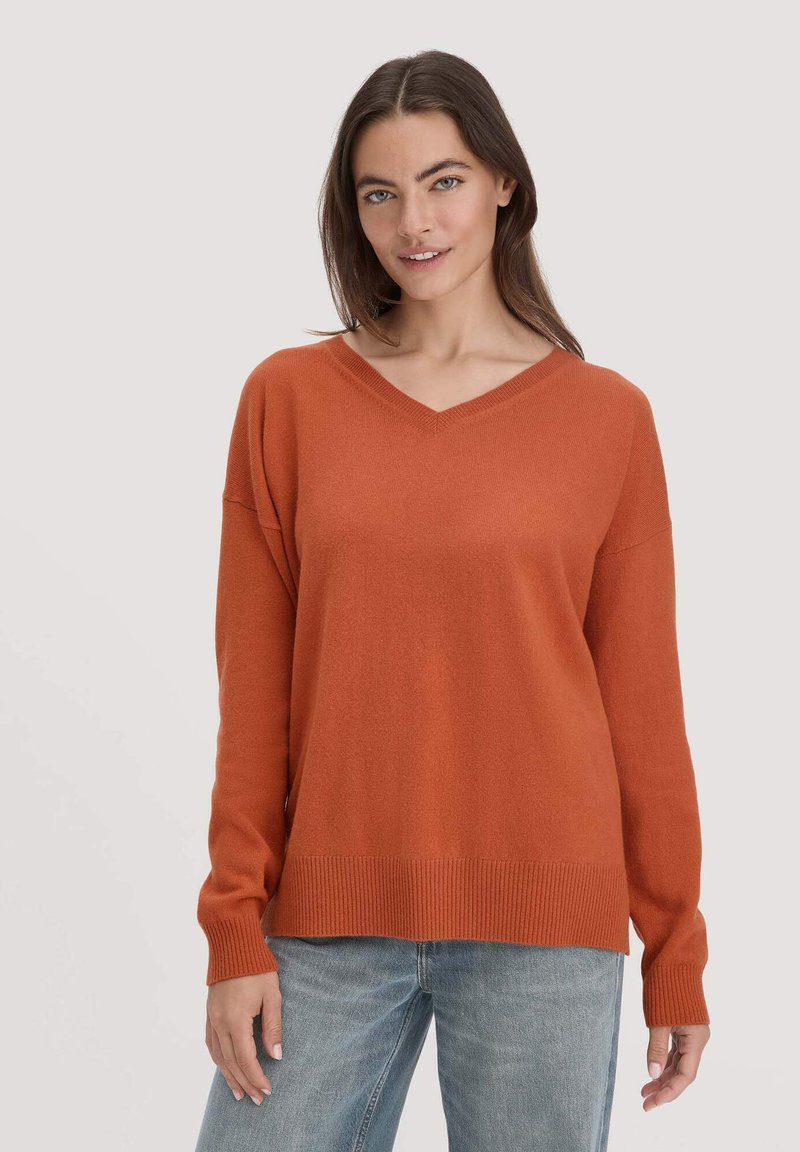 V-Ausschnitt, langärmliger Pullover in verbranntem Orange, aus weichem Strickstoff. Mit gerippten Bündchen und Saum, lockerer Passform und leicht fallenden Schultern.