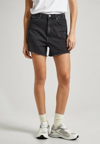 Pantalones cortos de mezclilla negra con dobladillo deshilachado, cintura alta, diseño de cinco bolsillos y herrajes plateados, combinados con zapatillas blancas y calcetines cortos claros.