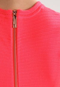 Haut ajusté en néon rose avec une texture côtelée et un col montant. Présente une fermeture éclair dorée au dos.