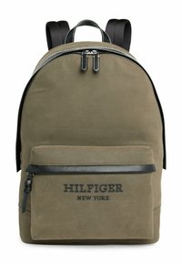 Zaino in tela verde oliva con accenti neri, doppia cerniera, una tasca frontale e il testo "HILFIGER NEW YORK" nella parte inferiore.