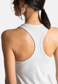 Débardeur dos nageur gris clair avec texture côtelée, présentant le design du dos et des détails sur les épaules. Le modèle a les cheveux attachés en une basse queue de cheval.