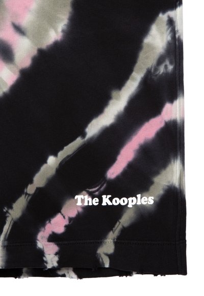 Sort stof med et tie-dye mønster i nuancer af pink og fløde. Har hvid tekst, der står "The Kooples" nær kanten.