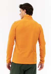 Oranžový fleece pulóver s vysokým golierom, dlhými rukávmi a hladkou textúrou. Obsahuje malé logo na dolnej časti chrbta.