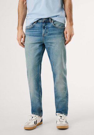 Jeans de mezclilla azul claro con un diseño de pierna recta, ligeras desgastadas y bolsillos. Combinados con zapatillas blancas y grises con suela de goma.