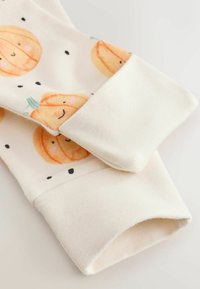 White fabric with ribbed cuffs and a pattern of smiling orange pumpkins with green stems and small black dots.