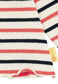 Pull rayé avec des bandes horizontales rouges, noires et blanches. Material en tricot doux avec un ourlet arrondi et une étiquette de marque jaune sur le côté.