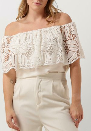 White off-the-shoulder top with lace overlay, featuring floral patterns, paired with high-waisted cream trousers in a smooth fabric.